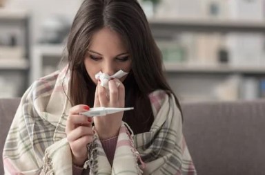 woman blowing nose and checking her temperature