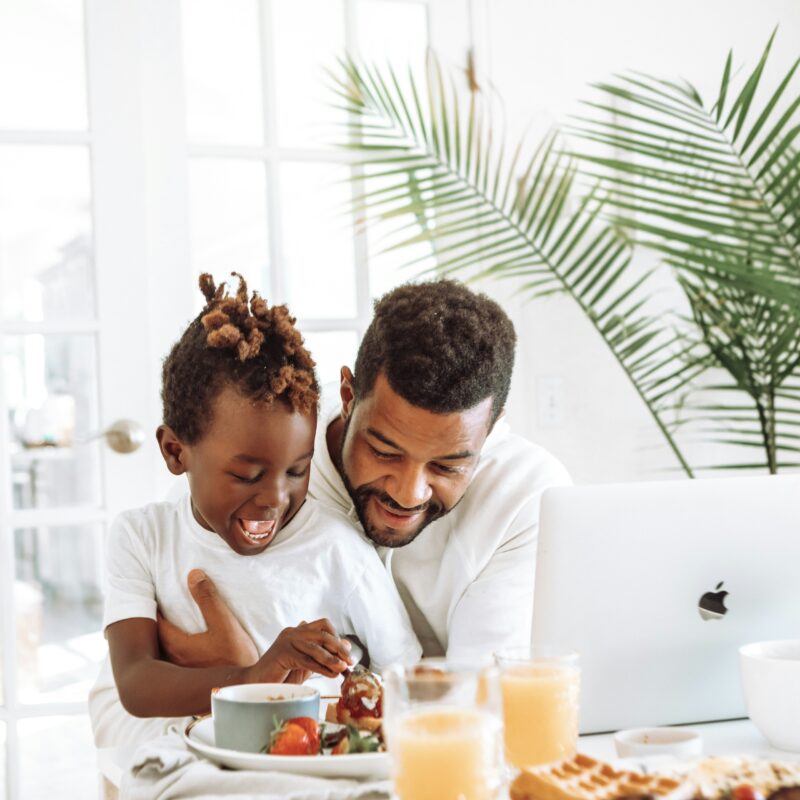 dad and son sitting in front of computer with breakfast